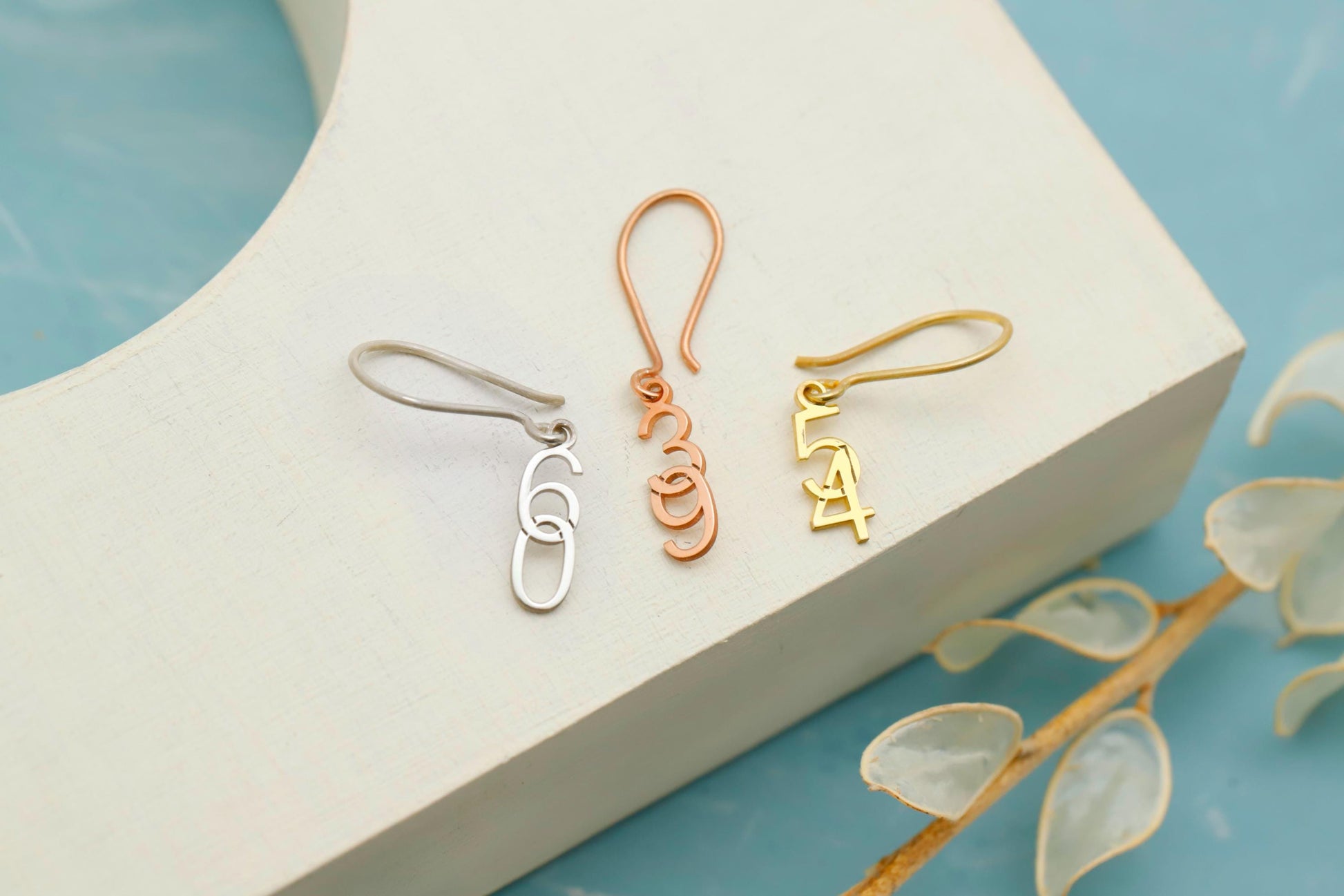 Three pairs of earrings on a white stand with a blue background