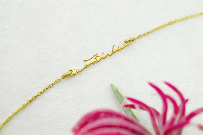 Gold chain on a light gray background with a pink flower.