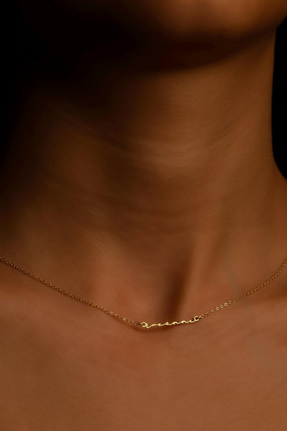A close-up image of a woman wearing a delicate gold-filled necklace with the name engraved on it.