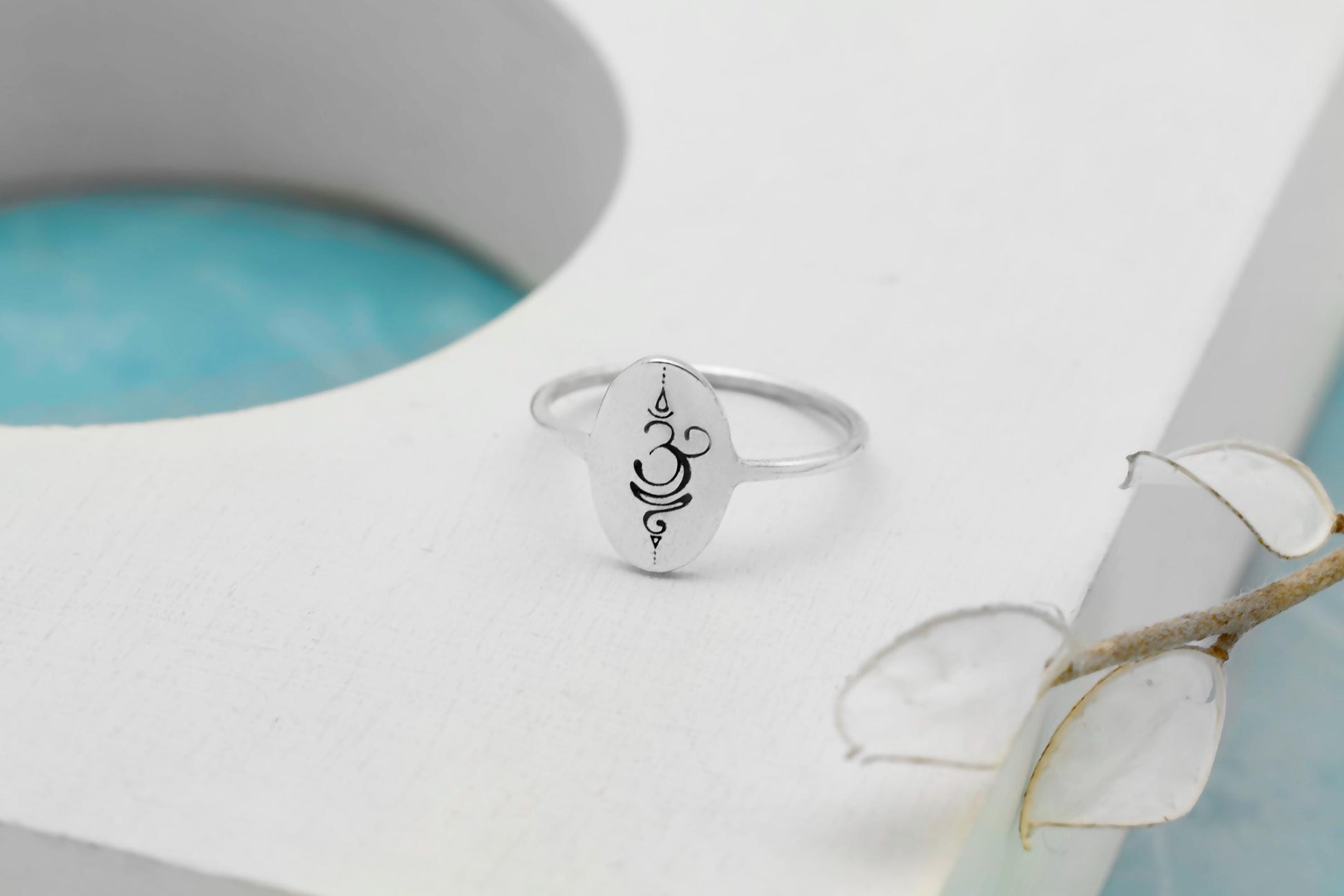 Silver ring with a symbol on a white surface with a light blue background