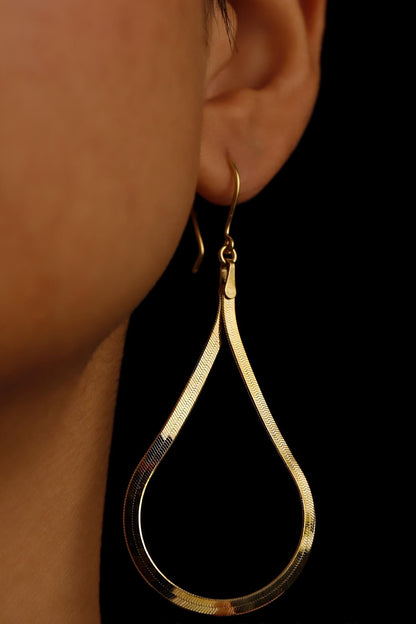 Gold hoop earring worn by a person against a dark background