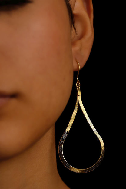 Gold teardrop earring worn by a person on a black background