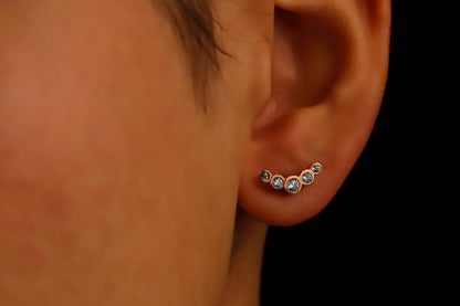 Close-up of an ear wearing a small earring with clear gemstones on a dark background