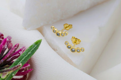 Gold earrings with small stones on a white surface with a pink flower.