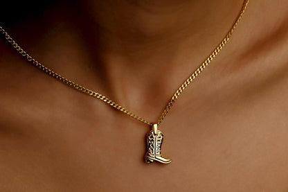 Gold necklace with a cowboy boot pendant on a person's neck.