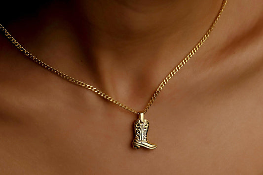 Gold necklace with a cowboy boot pendant on a person's neck.