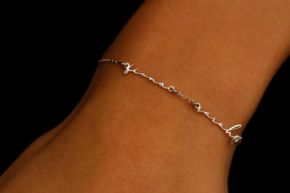 A gold personalized bracelet with two names, displayed on a person's wrist.