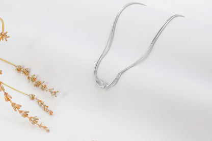 Three love knot bracelets made of 925 sterling silver, displayed in two different finishes, gold and rose gold, alongside decorative dried plants on a white background.