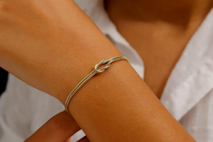 Three love knot bracelets made of 925 sterling silver, displayed in two different finishes, gold and rose gold, alongside decorative dried plants on a white background.