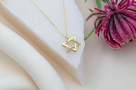 Gold necklace with a Star of David pendant on a person's neck against a dark background