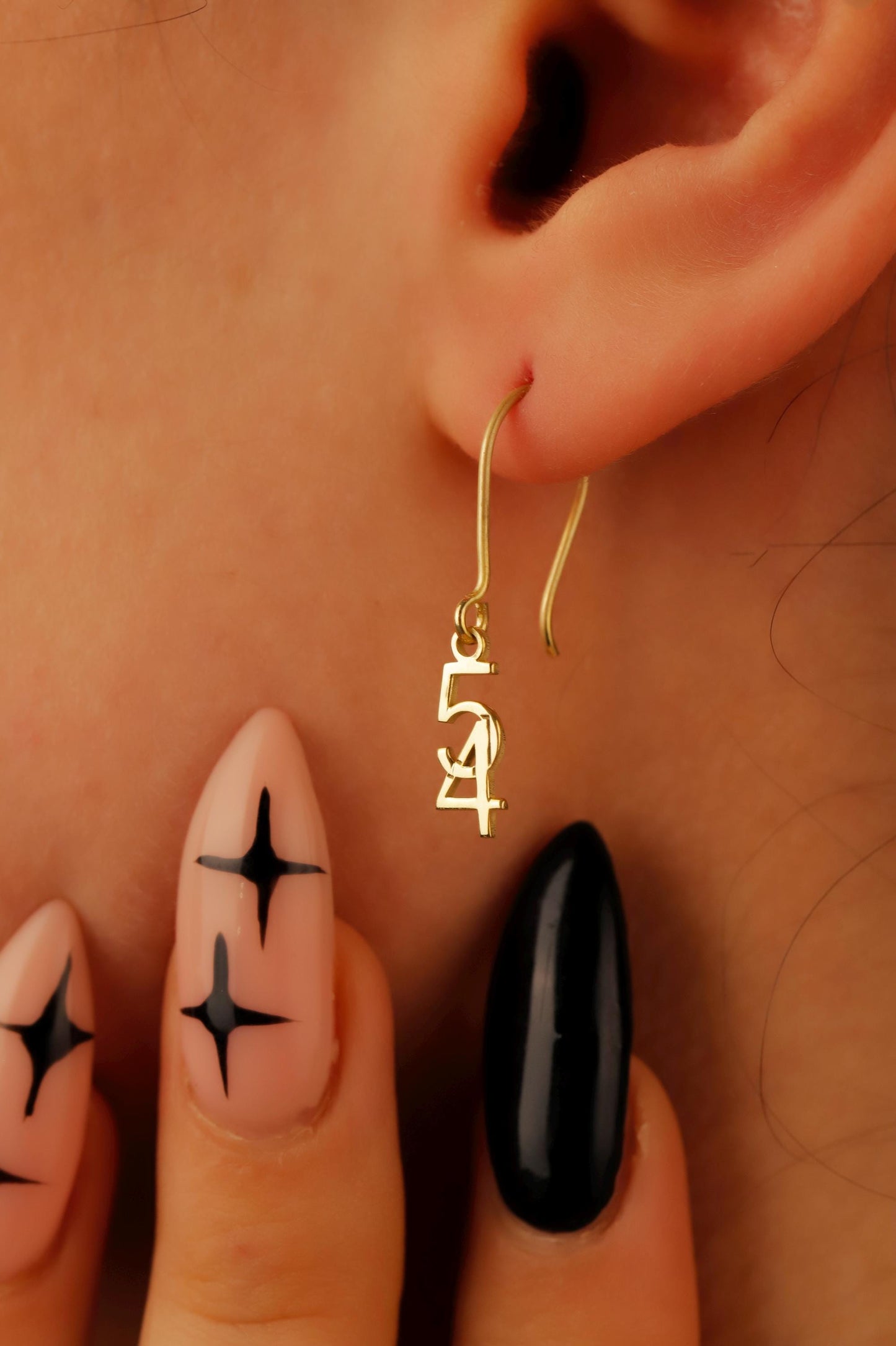 Gold hoop earrings worn by a person with black nail polish on their fingers.