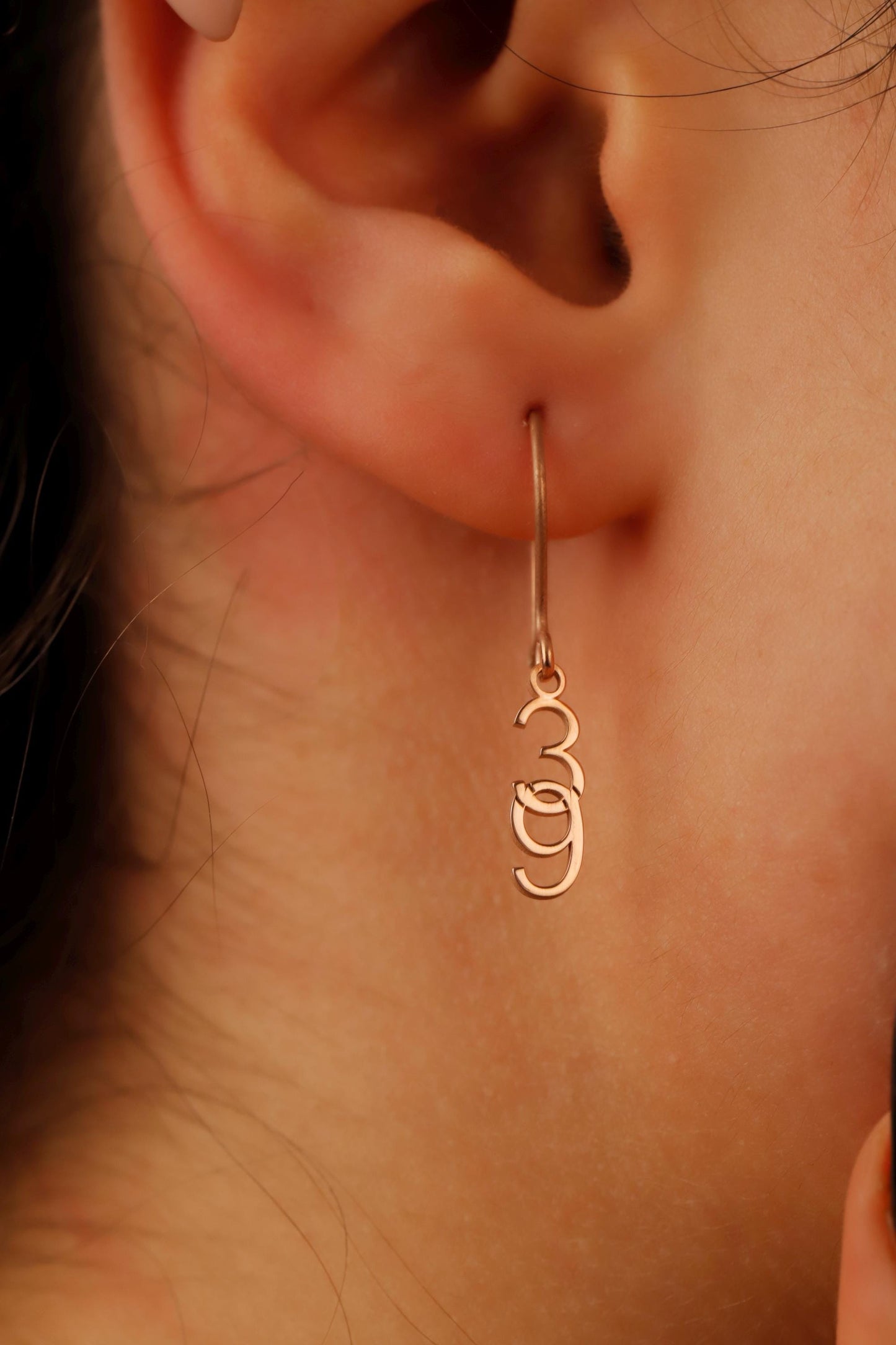Close-up of an ear wearing a gold hoop earring with a 'Om' symbol.