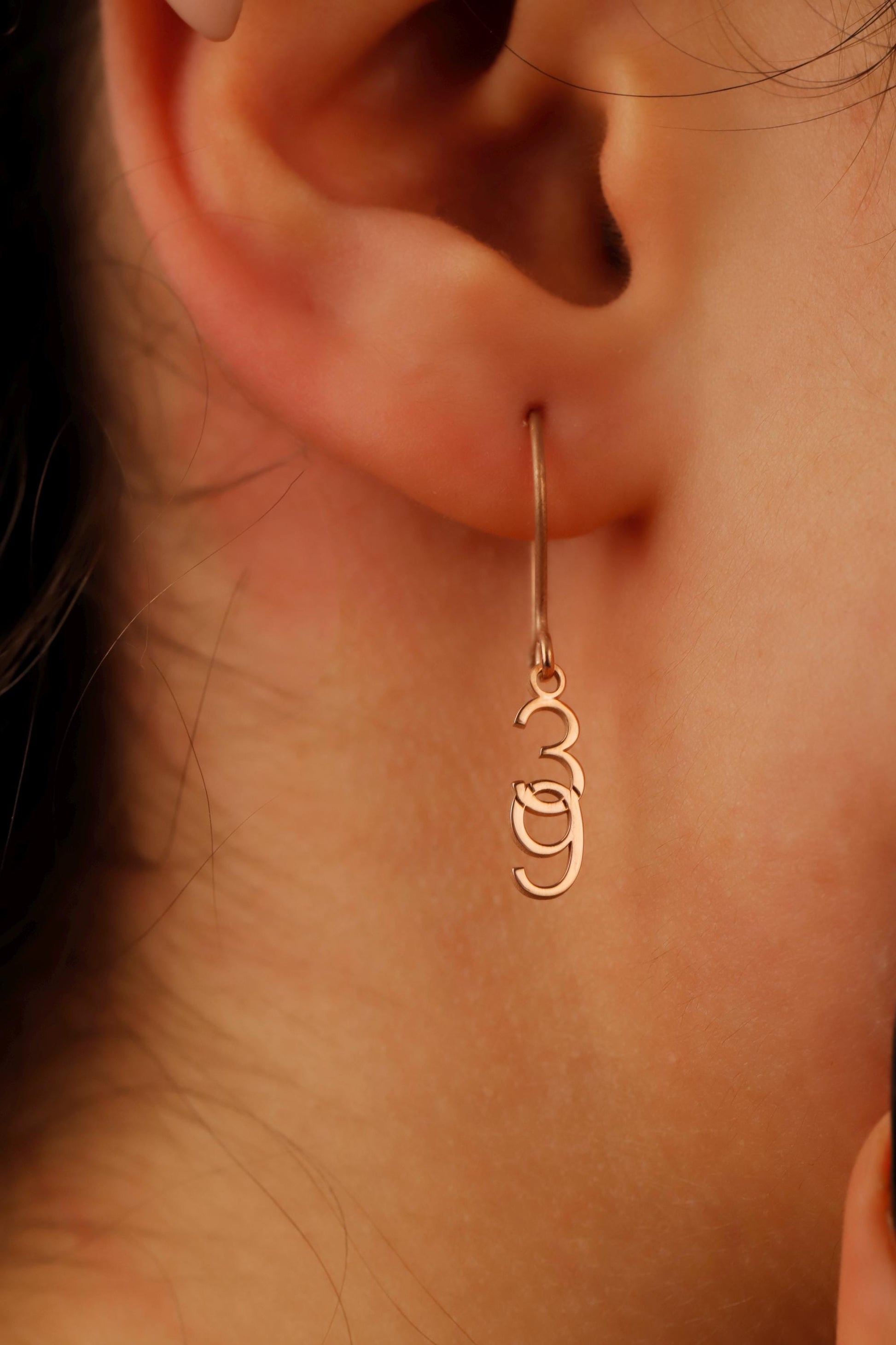 Close-up of an ear wearing a gold hoop earring with a 'Om' symbol.