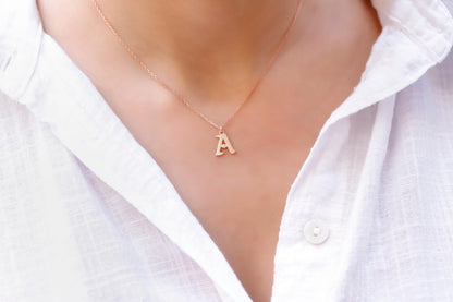 A person wearing a white shirt showcasing a dainty rose gold necklace with the initial 'A' on their neck.
