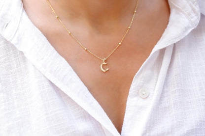 A person wearing a white shirt showcasing a dainty gold necklace with the initial 'E' on their neck.