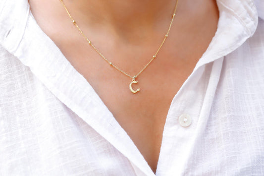 A person wearing a white shirt showcasing a dainty gold necklace with the initial 'E' on their neck.