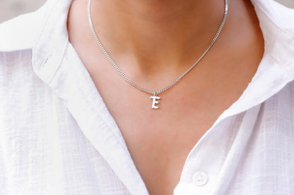 A person wearing a white shirt showcasing a dainty silver necklace with the initial 'E' on their neck.
