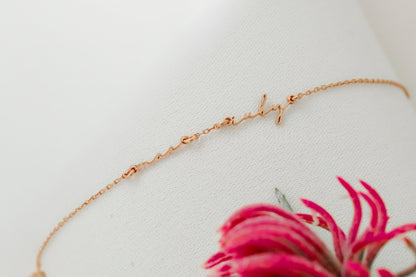 Rose gold necklace on a white surface with a pink flower in the foreground