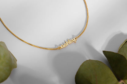  a dainty gold tiny name necklace with a box chain.