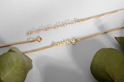  a dainty gold tiny name necklace with a box chain.
