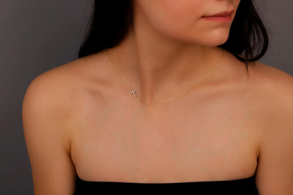 A woman wearing a gold sideways cross necklace with a cz diamond.