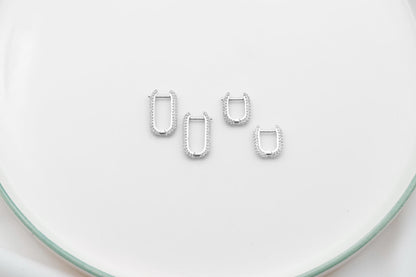 A close-up image of 2 silver diamond huggie hoop earrings.