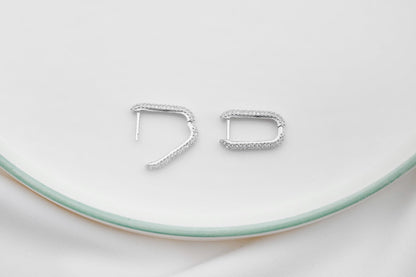 A close-up image of 2 silver diamond huggie hoop earrings.