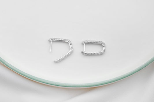 A close-up image of 2 silver diamond huggie hoop earrings.