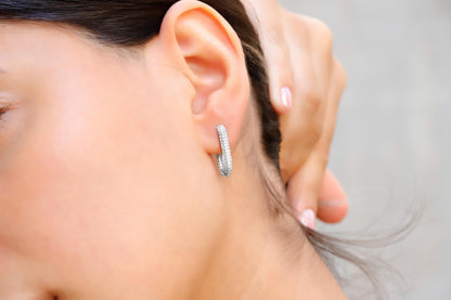 A close-up image of a woman's ear wearing a silver diamond huggie hoop earring.