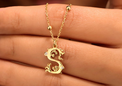 A close-up image of a gold initial necklace with a beaded ball chain, featuring a CZ stone on the initial pendant, worn by a person.