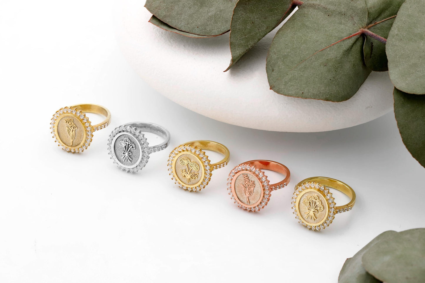 Set of gold and silver rings on a white surface with green leaves.