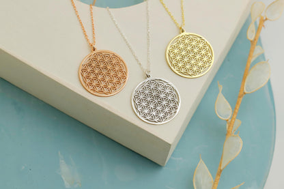 Three gold and silver necklaces with geometric pendants on a white box against a light blue background.