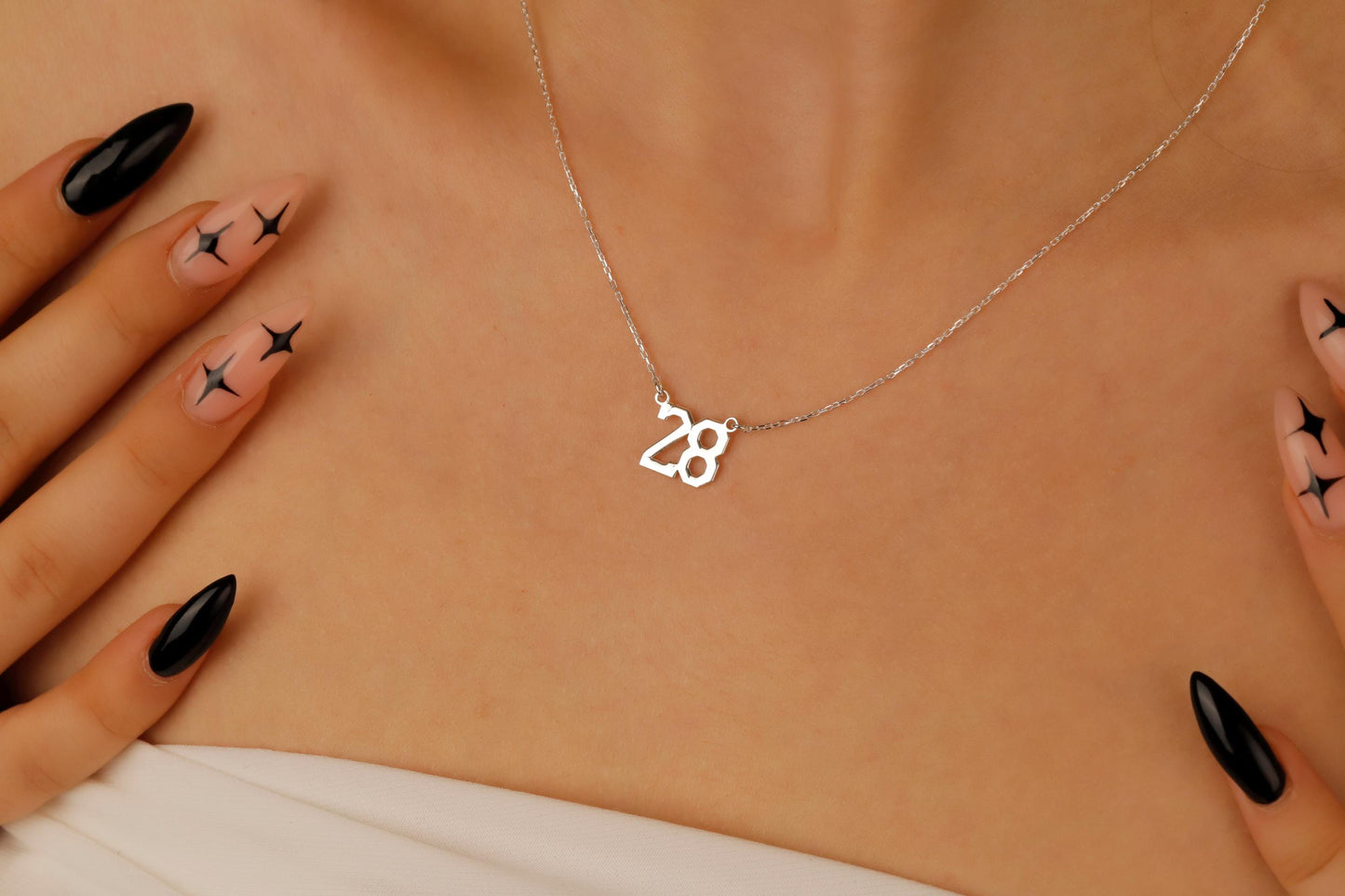 Necklace with a '28' pendant on a person's neck with black nail polish and star designs.