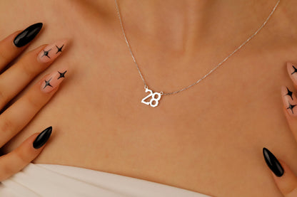 Necklace with a '28' pendant on a person's neck with black nail polish and star designs.