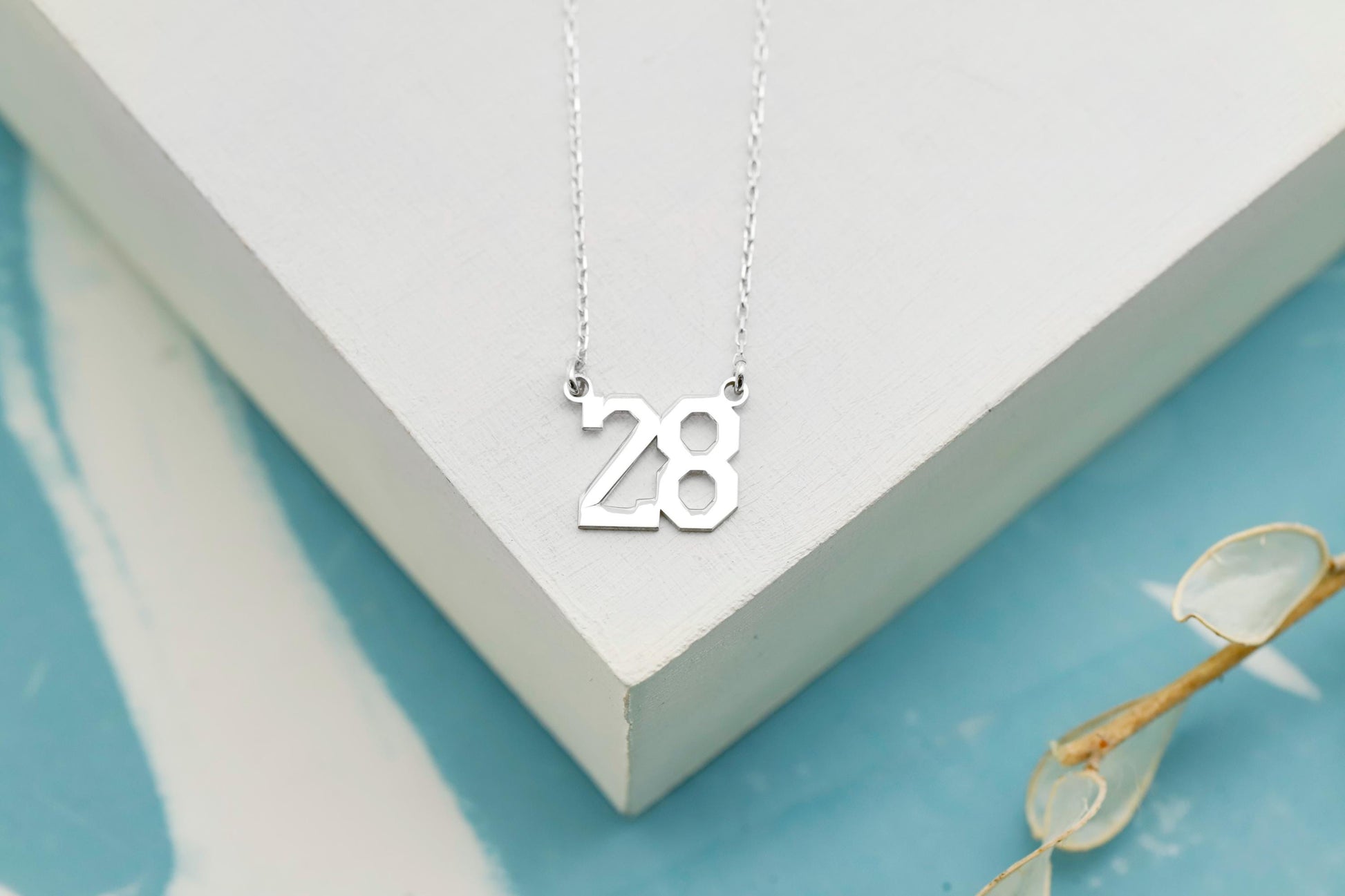 Silver necklace with the number '28' on a white surface