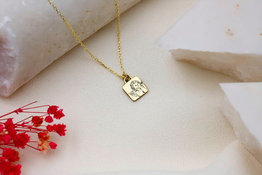 A close-up image of a gold-colored necklace with a personalized pendant, displaying the engraved text 'guardian angel' on a person's skin.