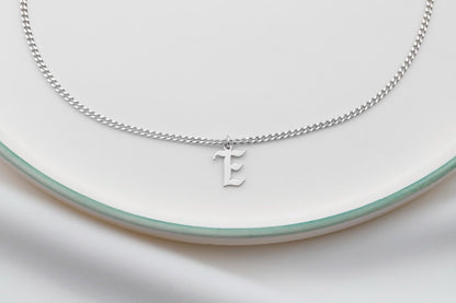 picture showcasing a dainty silver necklace with the initial 'E' on their neck.