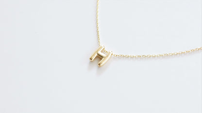 A close-up image of a a gold-filled balloon necklace with a single letter 'H' pendant.