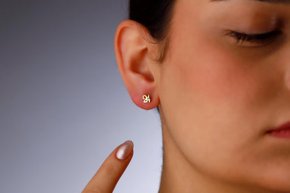 A close-up image of a woman's ear wearing a gold stud earring with a dainty number design.