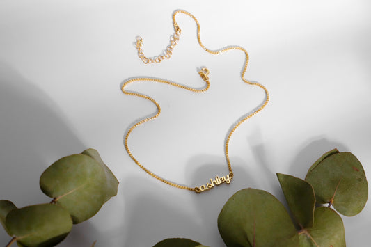  a dainty gold tiny name necklace with a box chain.