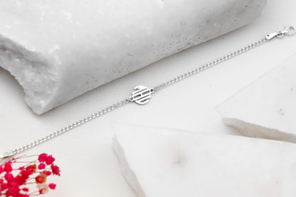 A close-up image of a wearing a SILVER bracelet with a block monogram initial pendant.