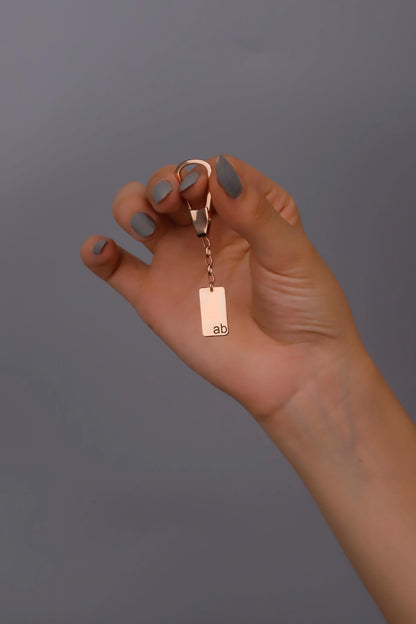 A hand holding a silver dog tag key chain with a plain design.