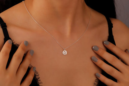 A person wearing a dainty silver monogram necklace on a delicate chain, placed over a low-cut neckline.