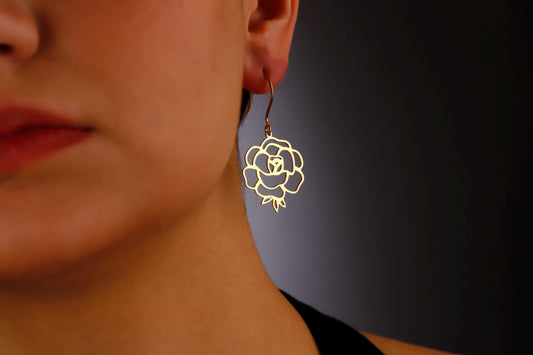 A woman wearing a gold floral dangle earring.