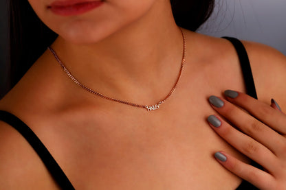 A woman wearing a dainty personalized name necklace with an intertwined design in silver, displayed on a choker-length chain.