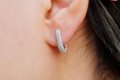 A close-up image of a woman's ear wearing a silver diamond huggie hoop earring.