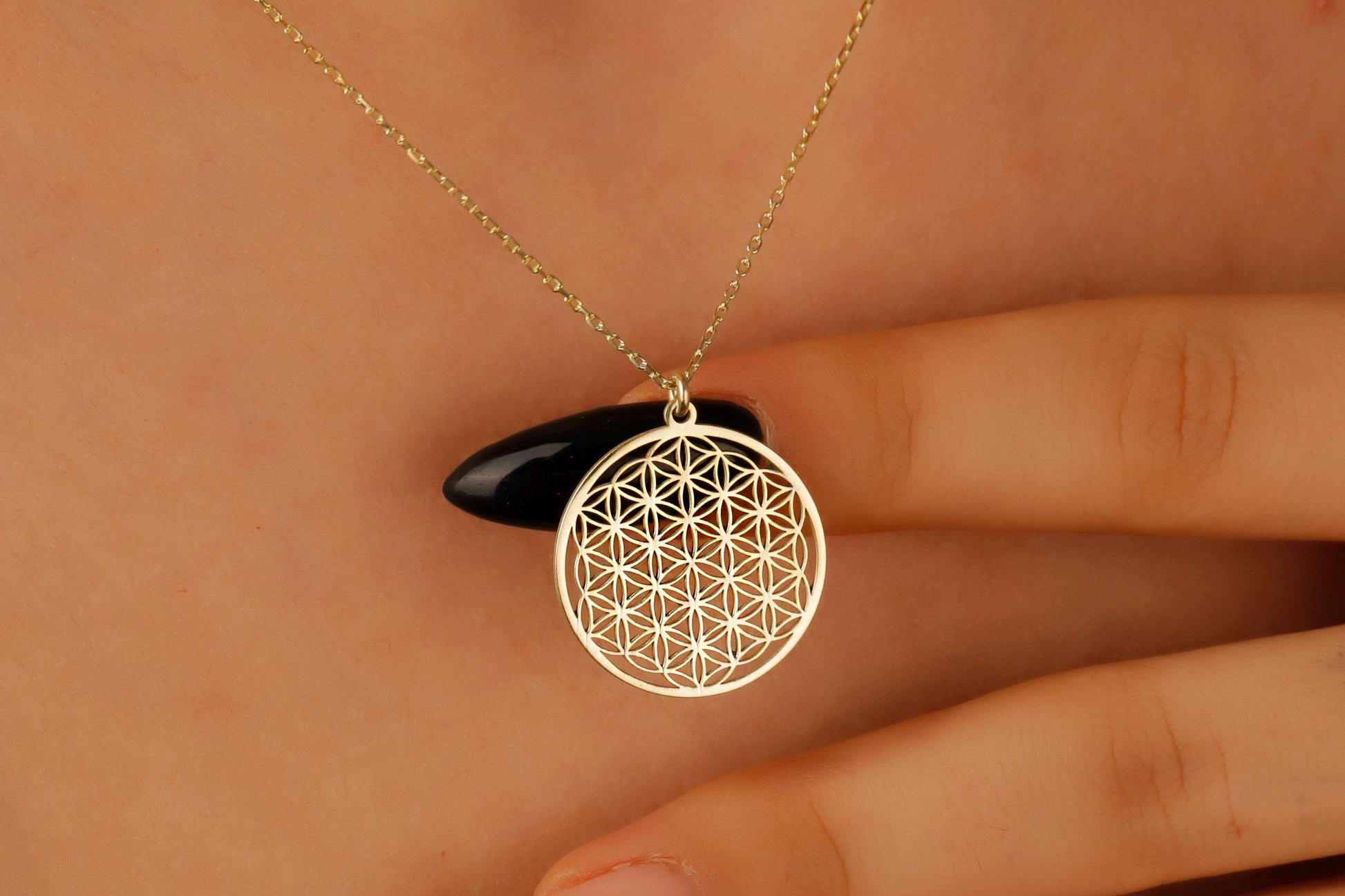 Gold necklace with a geometric pendant held by a hand against a neutral background