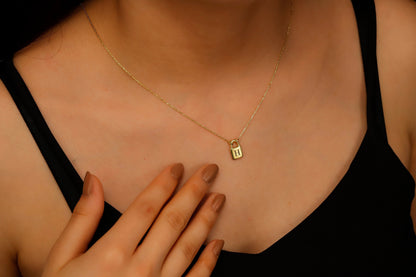 A close-up image of a person wearing a padlock-shaped pendant necklace in gold color, attached to a chain.