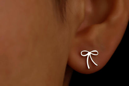 Silver bow-shaped earring on a person's ear with a black background