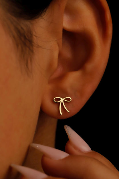 Close-up of an ear with a gold bow-shaped earring against a dark background